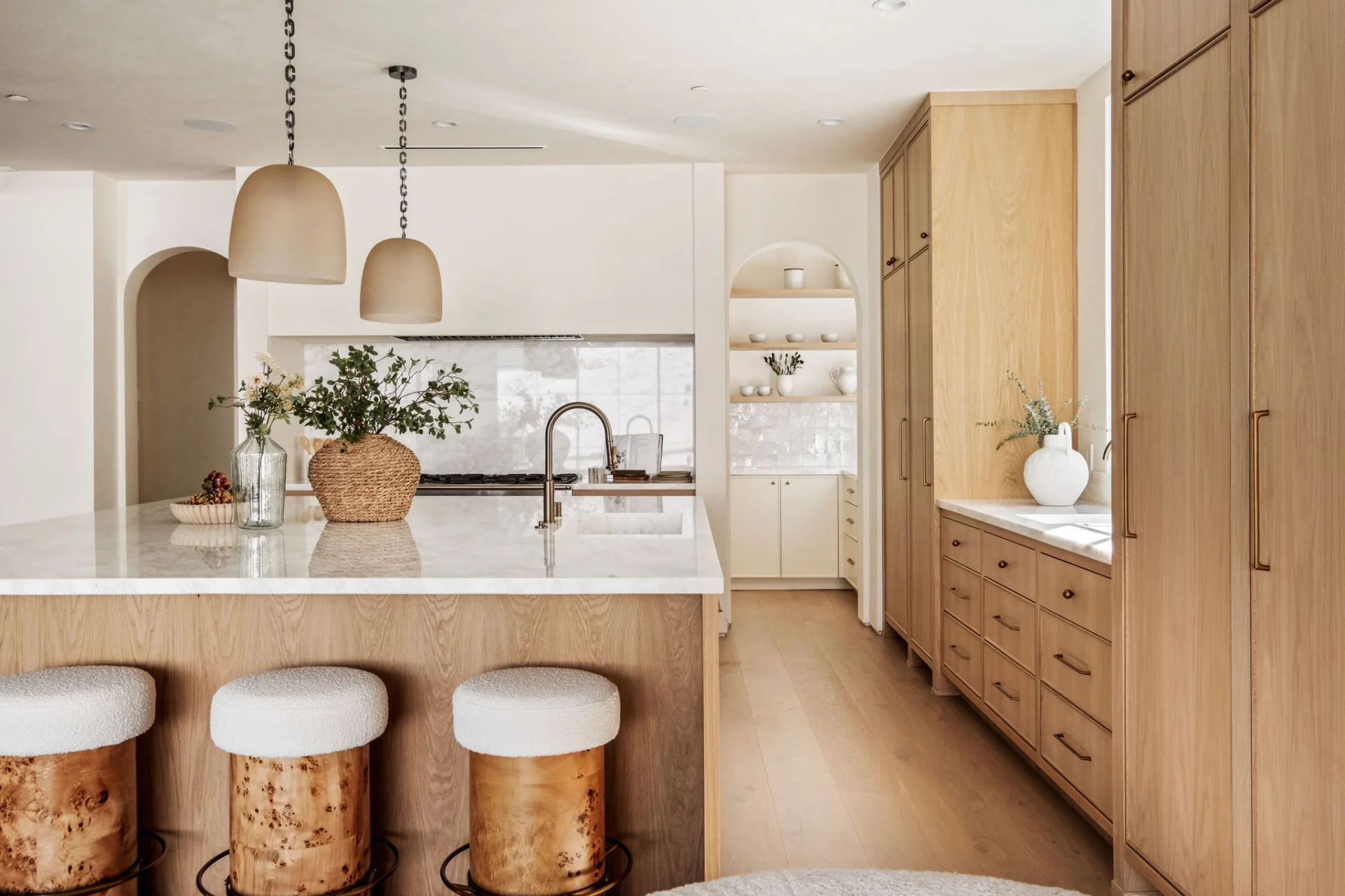 White oak kitchen with marble island, arched pantry nook and bouclé counter stools
