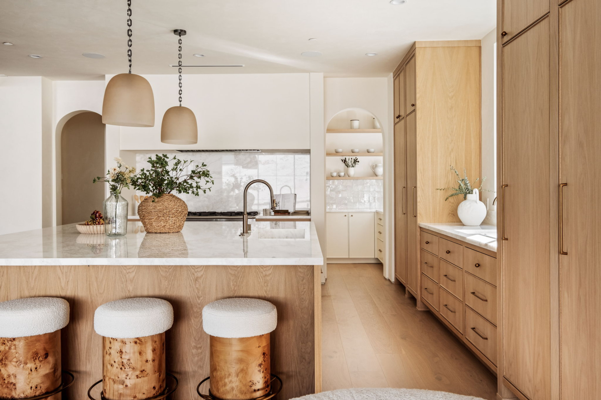 White oak kitchen with a marble waterfall island, brass fixtures, ceramic pendants and zellige-tiled butler's pantry