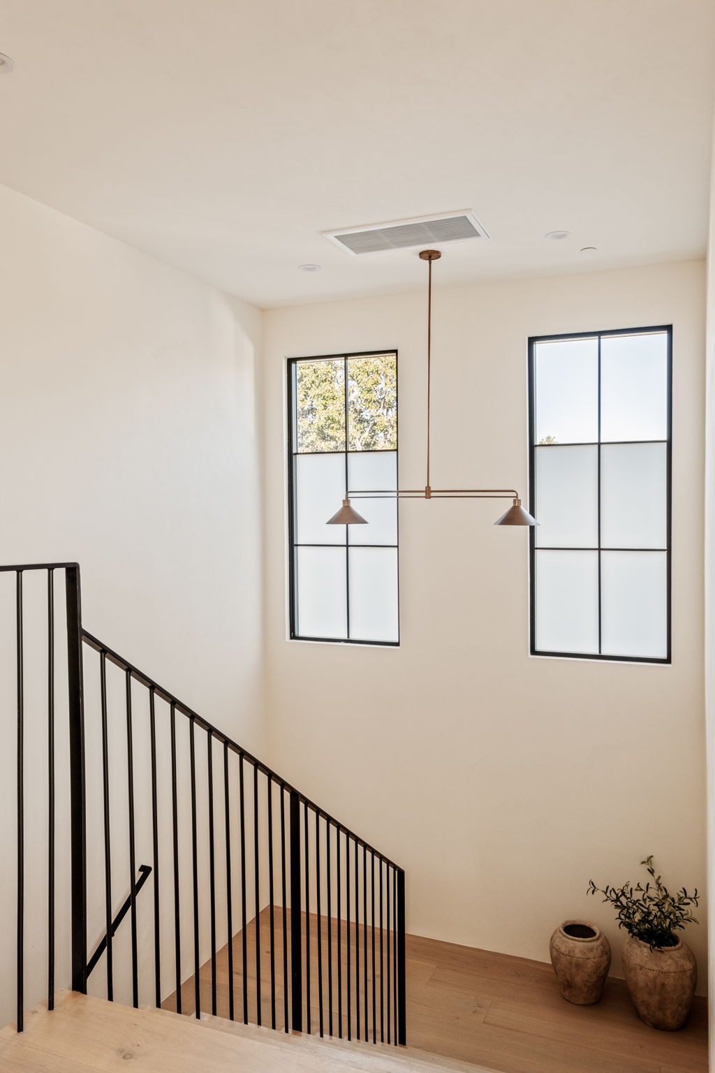 Stair hall with steel windows, a bronze linear pendant and terracotta olive pots