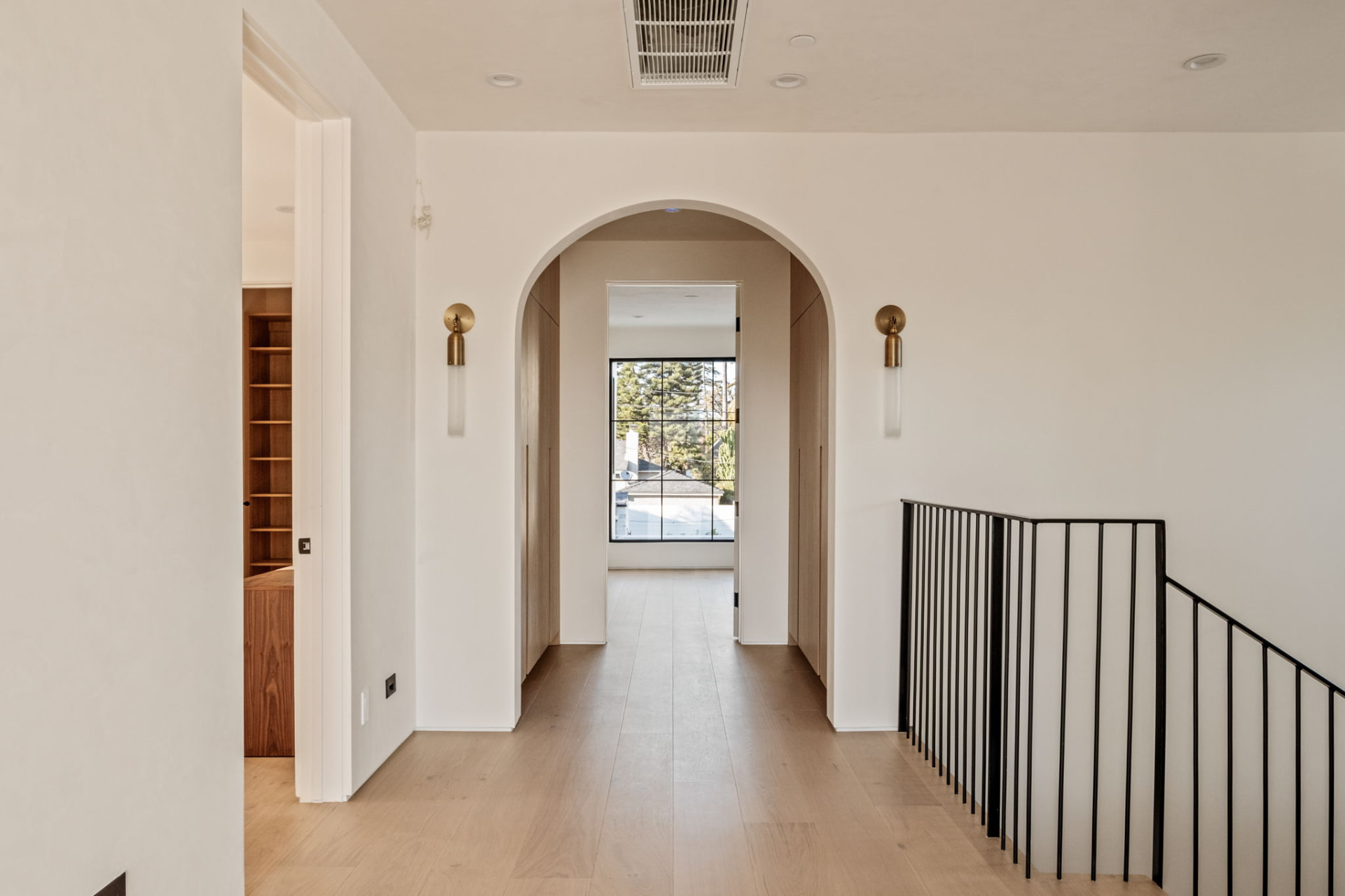 Upstairs landing with an arched plaster opening, brass sconces and a black steel railing