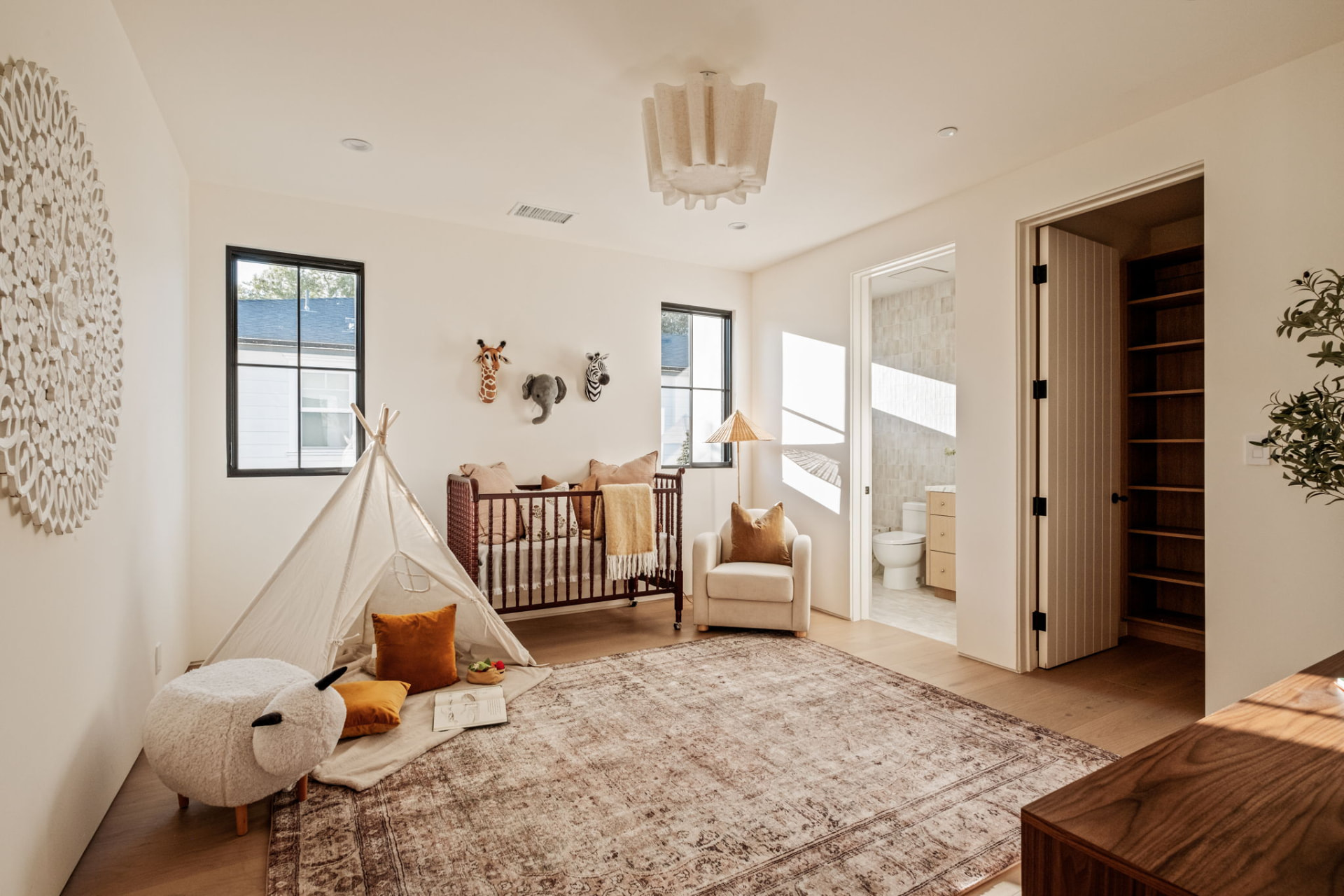 Nursery with a canvas teepee, spindle crib, plaster chandelier and vintage rug beside an ensuite bath