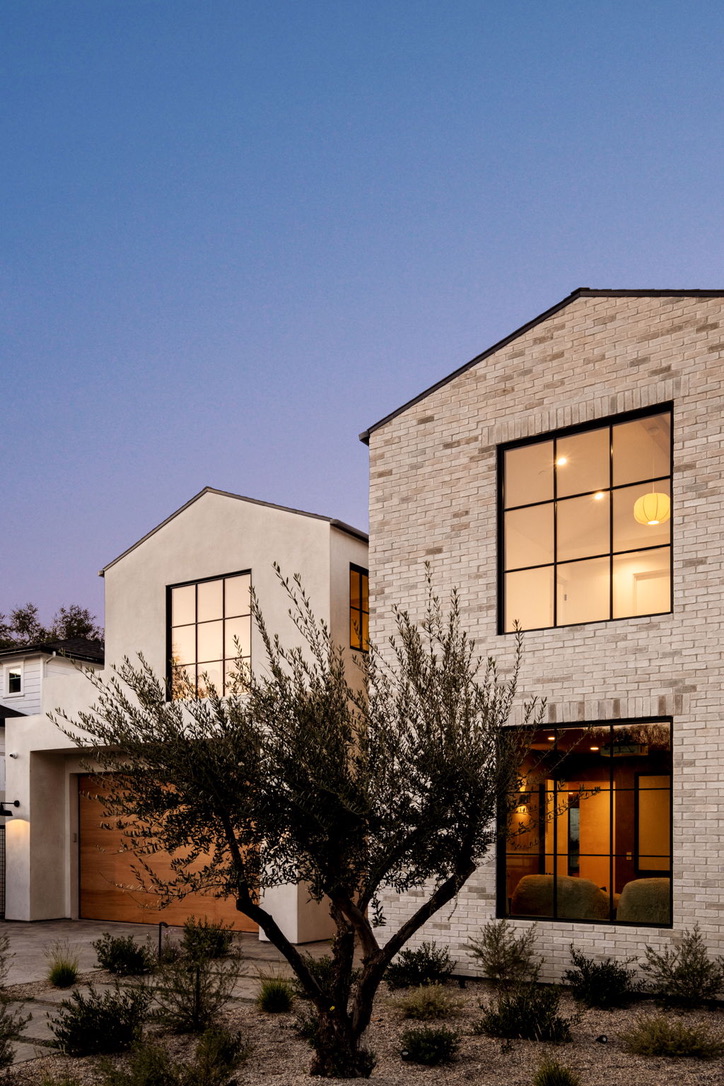 Gabled white brick and stucco home at blue hour framed by a mature olive tree and drought-tolerant planting