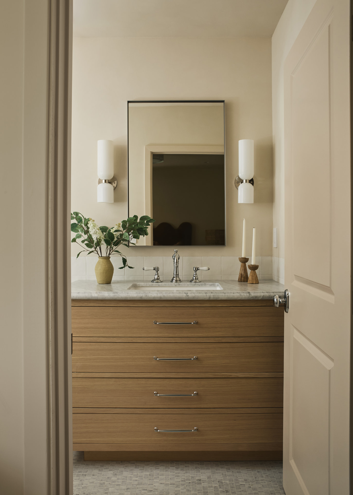 Powder room with an oak vanity, marble counter, slim mirror and opal glass sconces