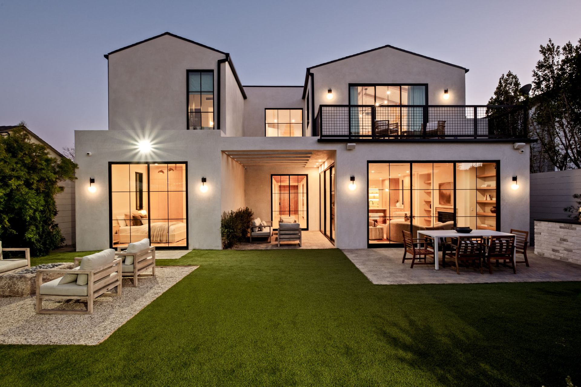 Rear elevation at dusk with stucco gables, black steel doors and a lawn terrace
