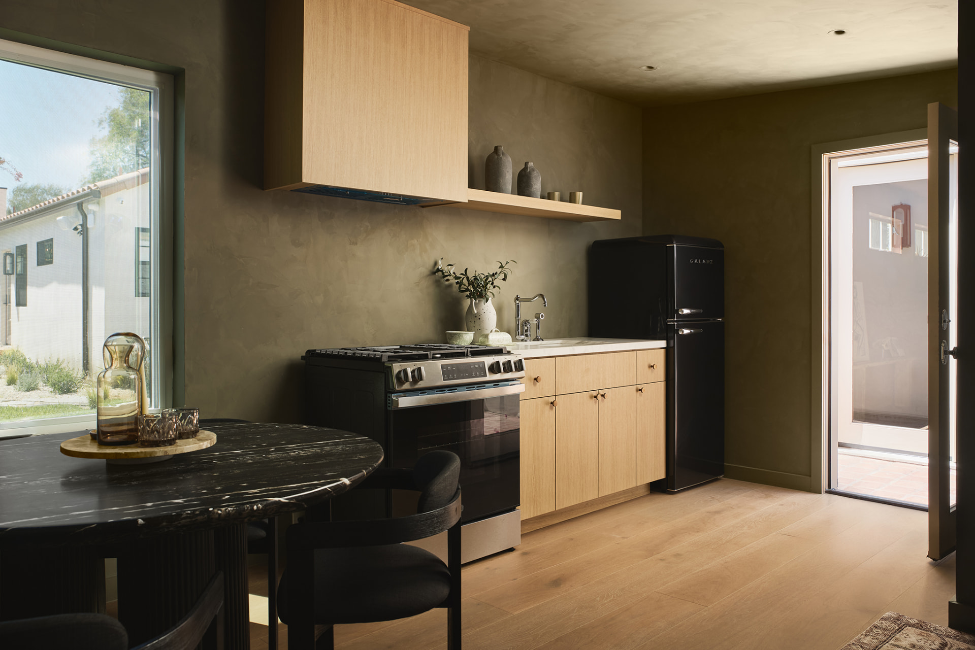 ADU kitchenette with white oak cabinetry, olive limewash walls, black retro refrigerator and garden window