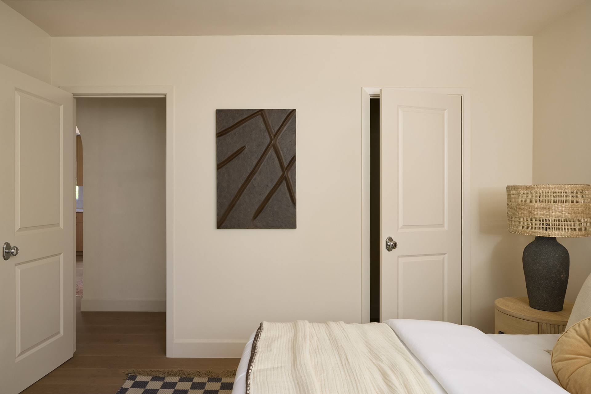 Bedroom with a textured dark artwork, woven lamp and checkered runner on oak floors