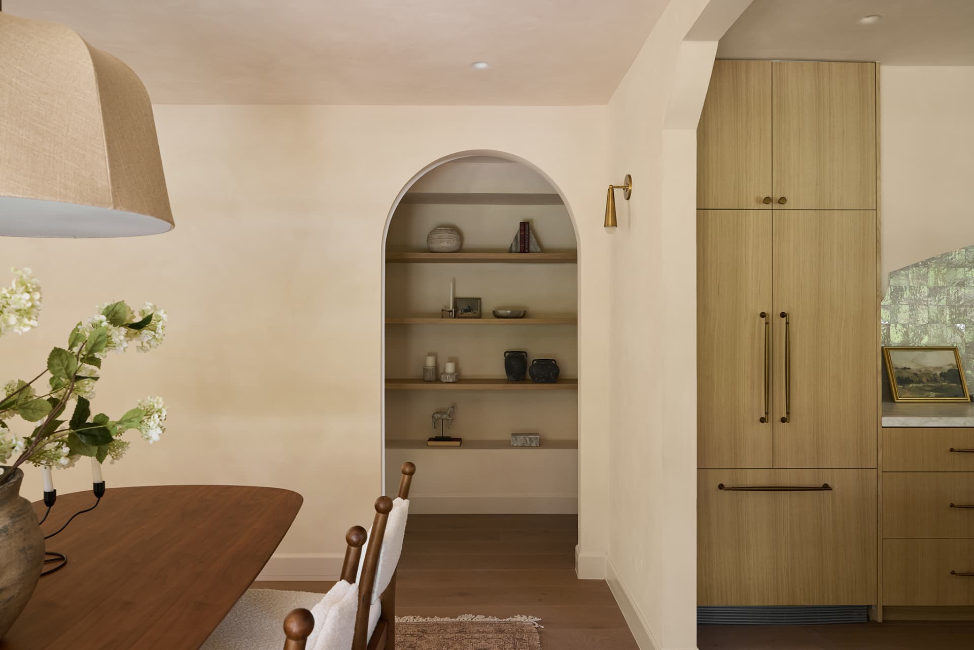Arched built-in shelving beside a white oak paneled refrigerator wall
