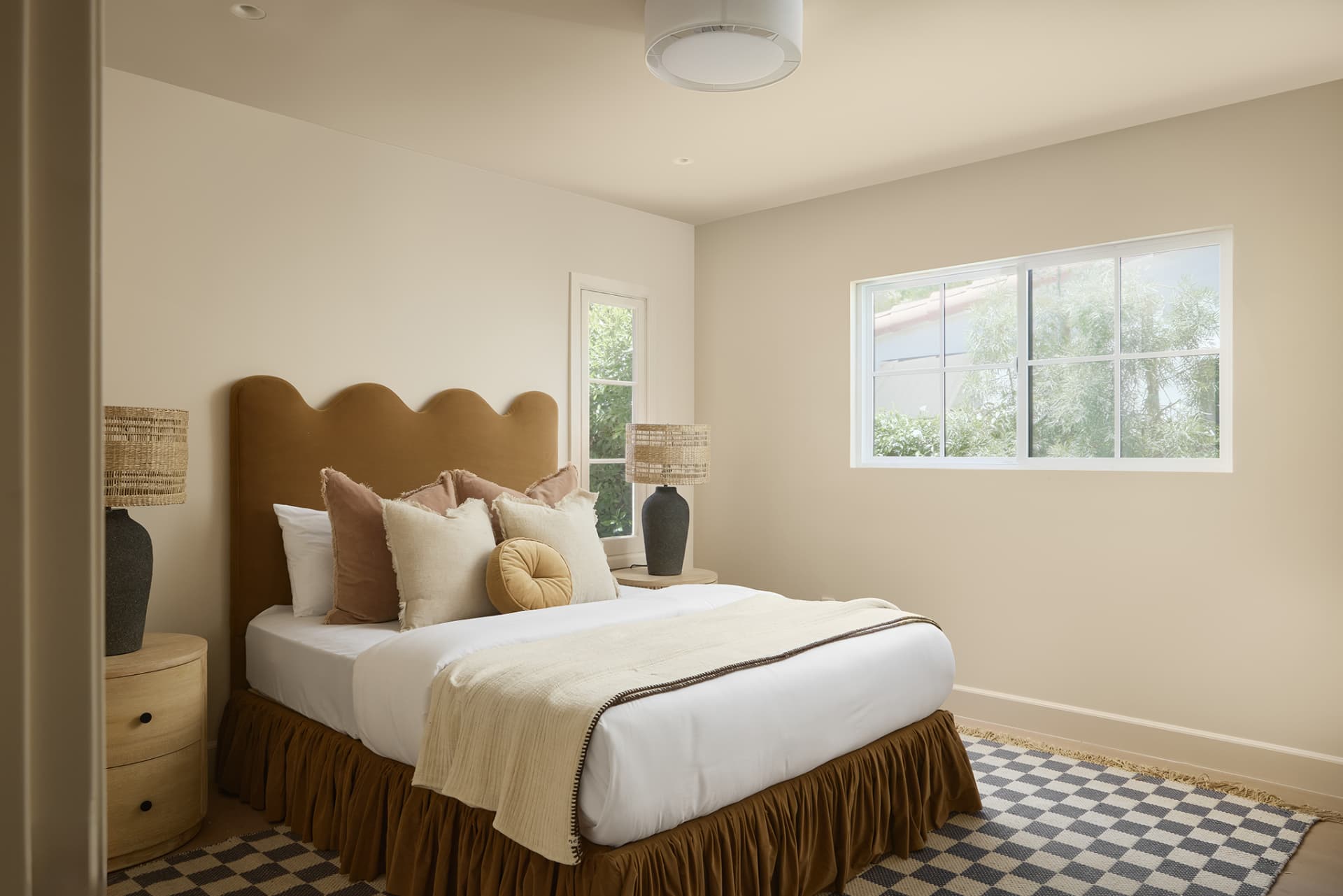 Guest bedroom with scalloped velvet headboard, woven lamps and checkered rug
