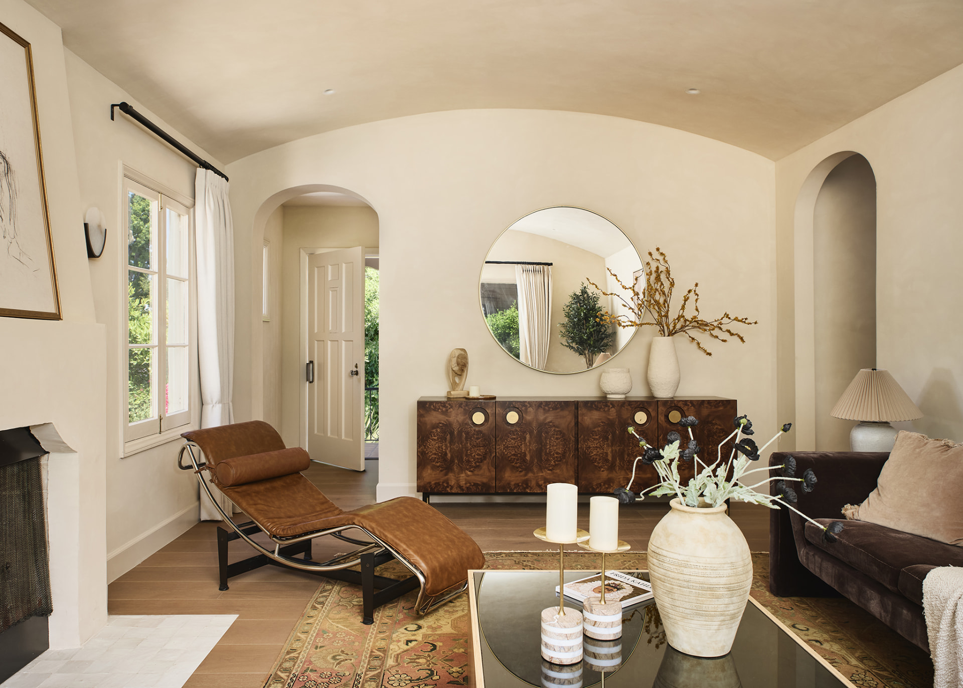 Vaulted plaster living room with arched openings, burl credenza and round brass mirror