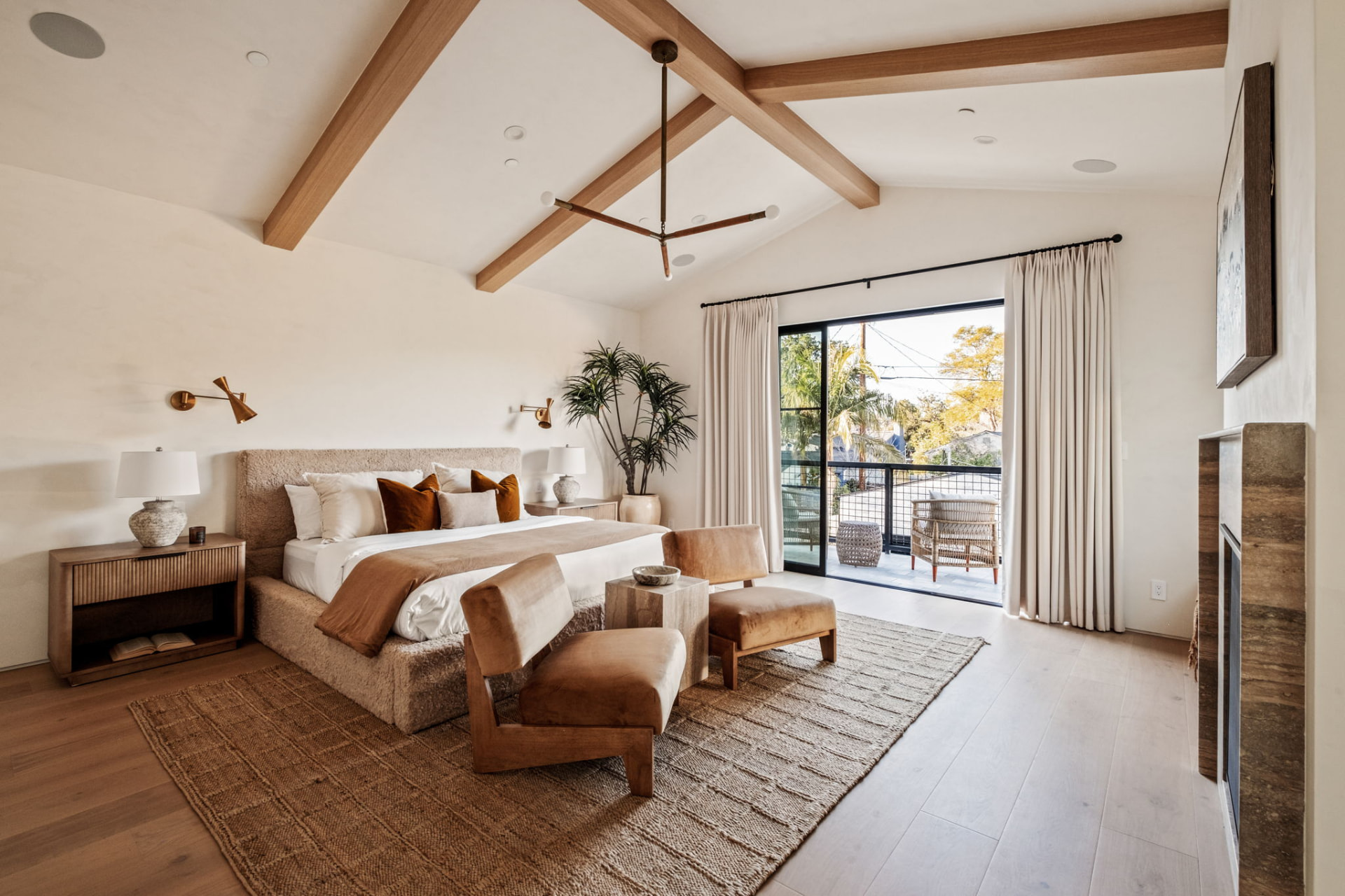 Primary suite with exposed oak trusses, brass sconces and sliding steel doors onto a private balcony