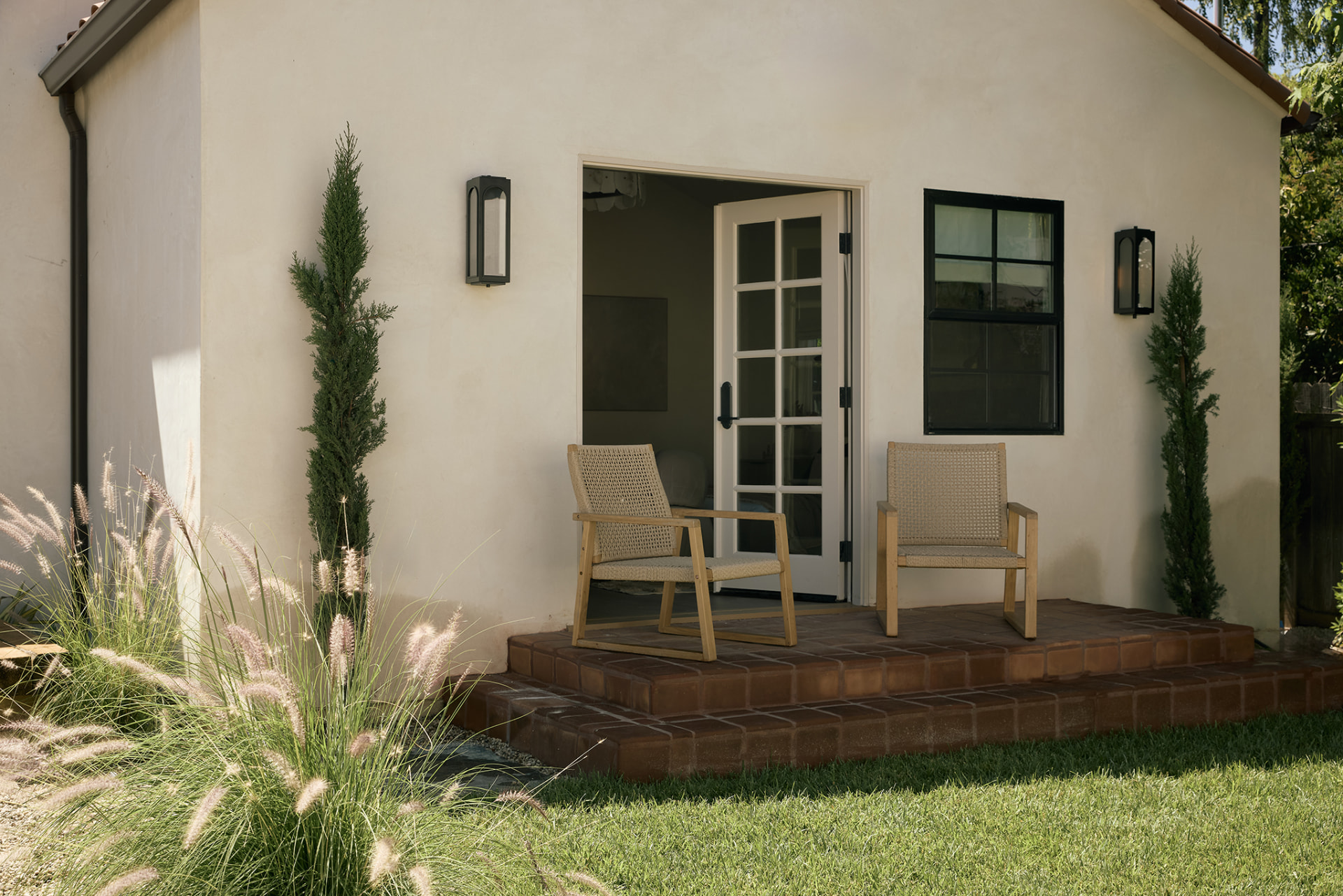 Spanish-style guest house exterior with brick patio, French doors and cypress trees