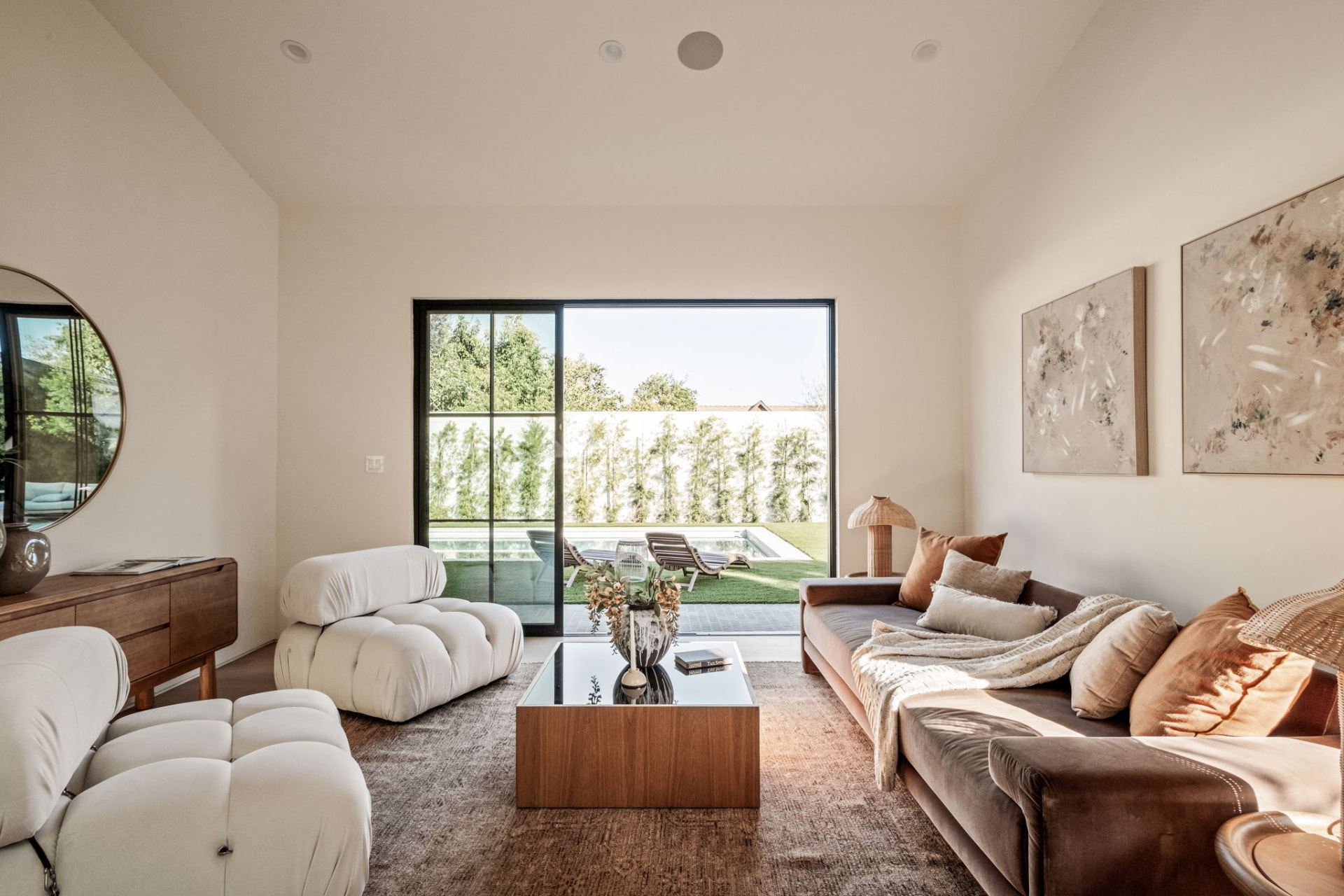 ADU living room with vaulted ceiling, sliding steel doors opening to the pool and bouclé seating