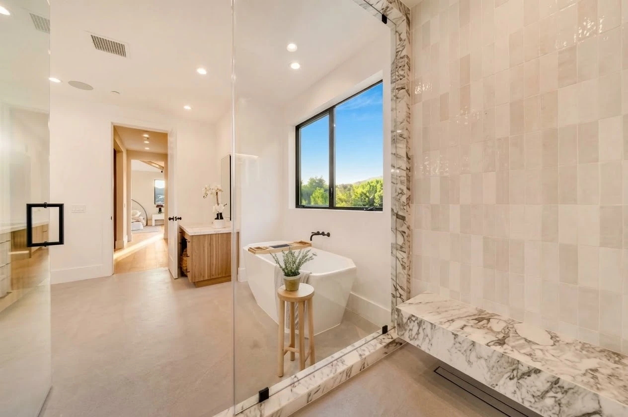 Primary bathroom with a freestanding tub, oak vanity and marble-trimmed glass shower