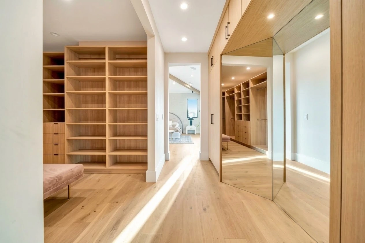 Walk-in closet with custom oak shelving, mirrored wardrobe doors and oak floors