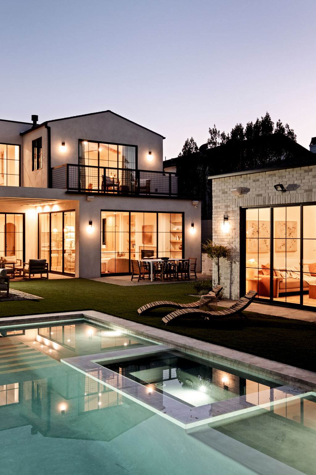 Evening view across the pool and spa toward the lit dining terrace and brick pavilion