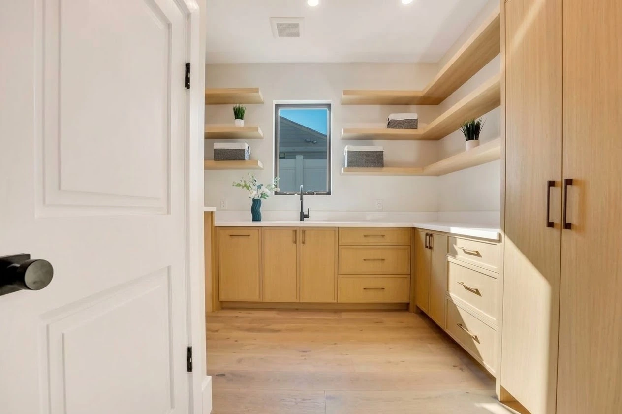 Prep kitchen with oak cabinetry, open shelving, white counters and a black faucet beneath a narrow window