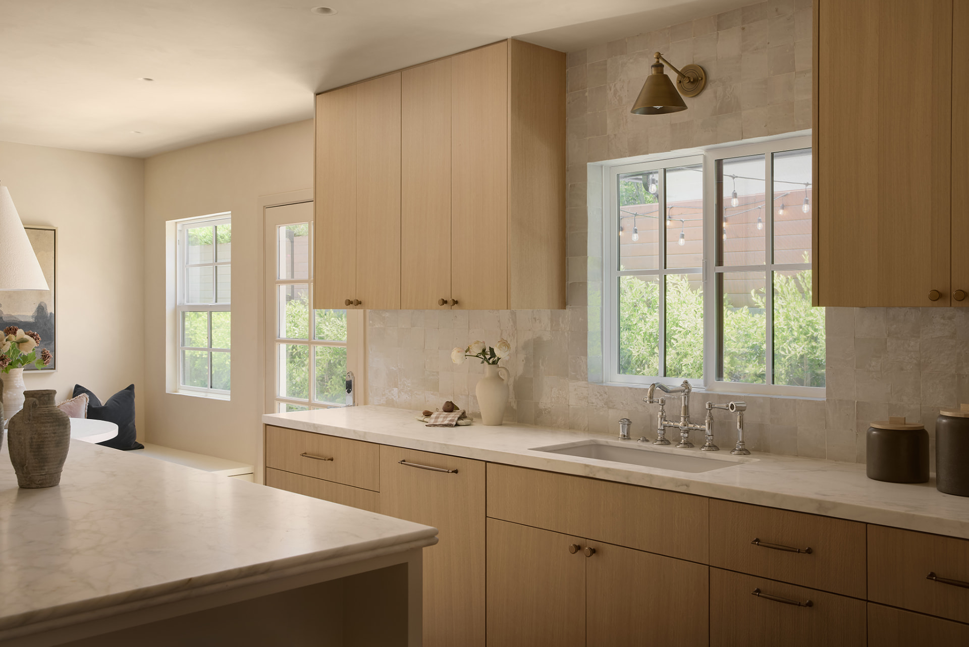 Kitchen with white oak cabinetry, marble counters, garden windows and an aged brass sconce