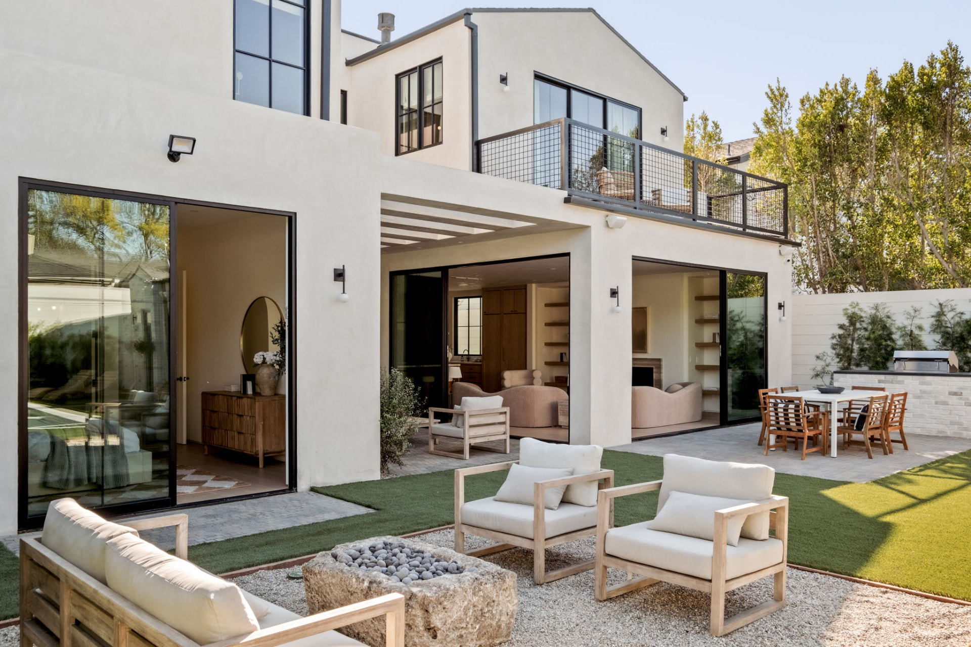Rear elevation with pocketing glass walls, a pergola-covered patio terrace, balcony and a stone fire pit lounge on the pool garden