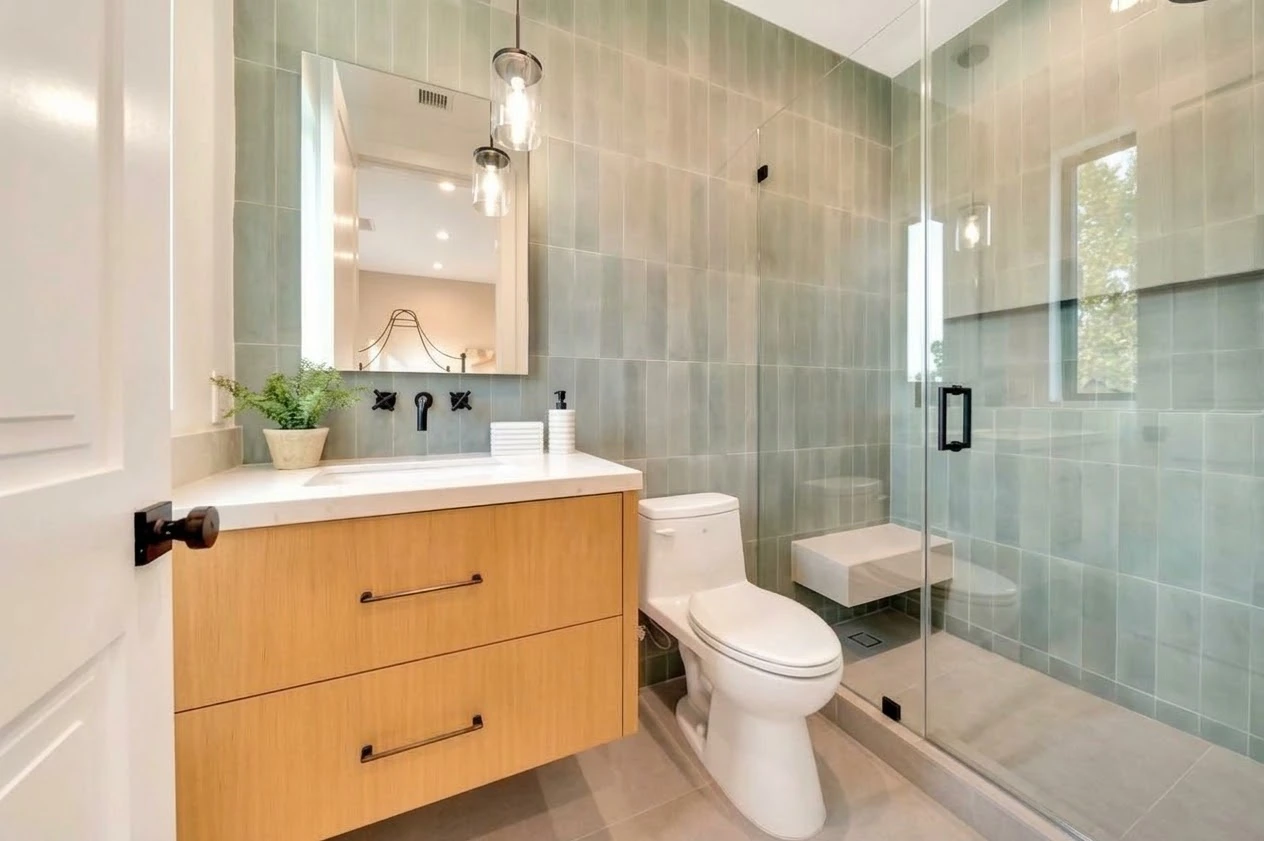 Bathroom with green tile walls, a floating oak vanity and a glass-enclosed shower with black fixtures
