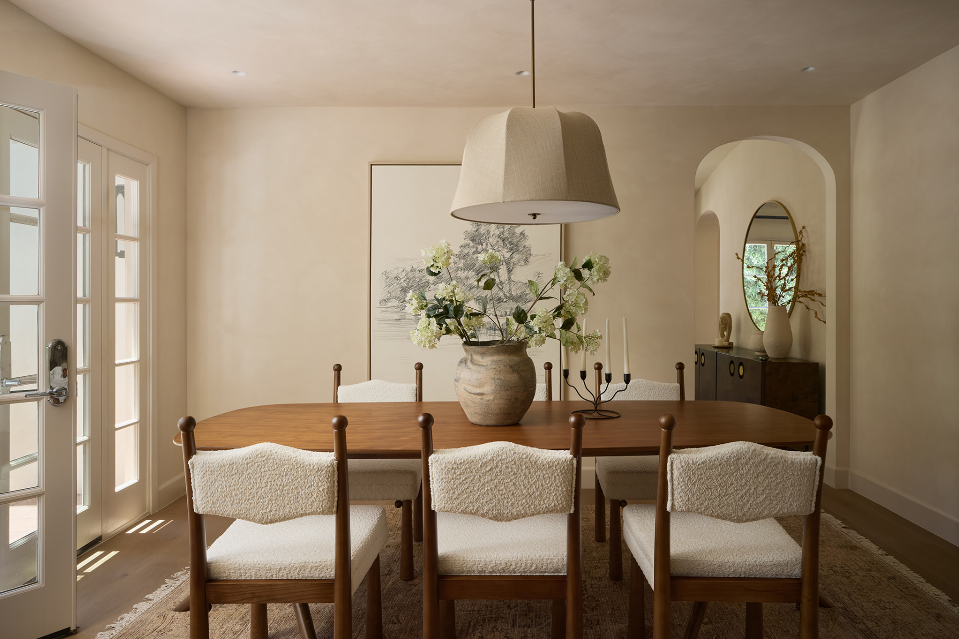Dining room with walnut table, bouclé chairs and an arched niche beyond
