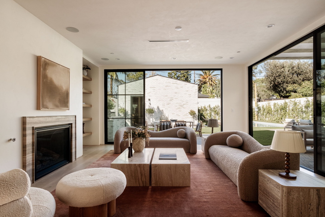 Living room with a travertine fireplace and corner sliding glass walls opening onto a pool garden