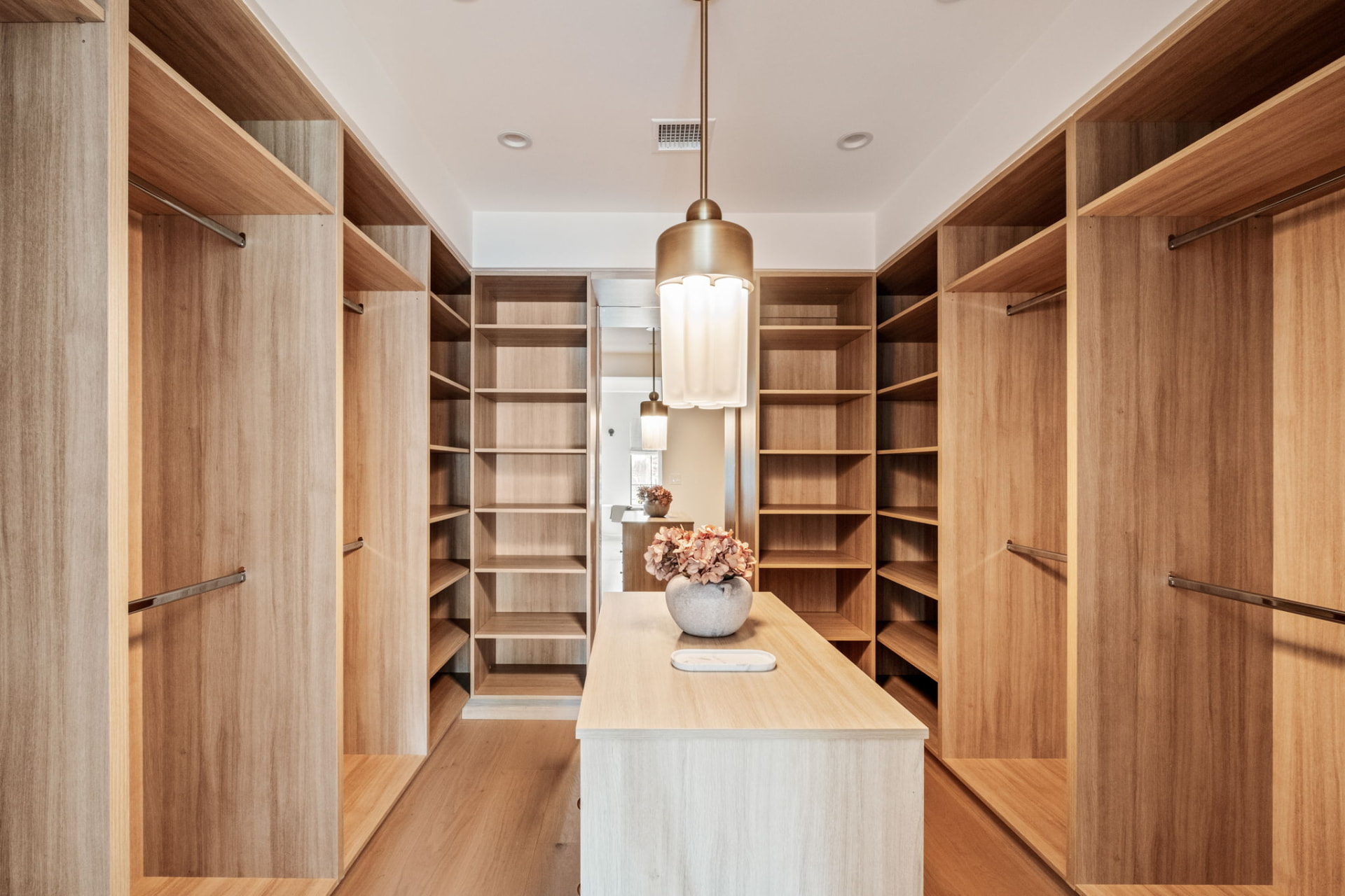 Walk-in closet with white oak shelving, a center island and a brass pendant