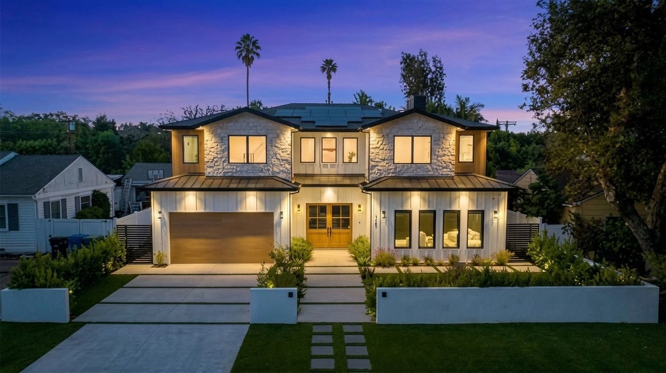 Front elevation at twilight with illuminated stone gables, white siding, oak garage door and landscaped entry