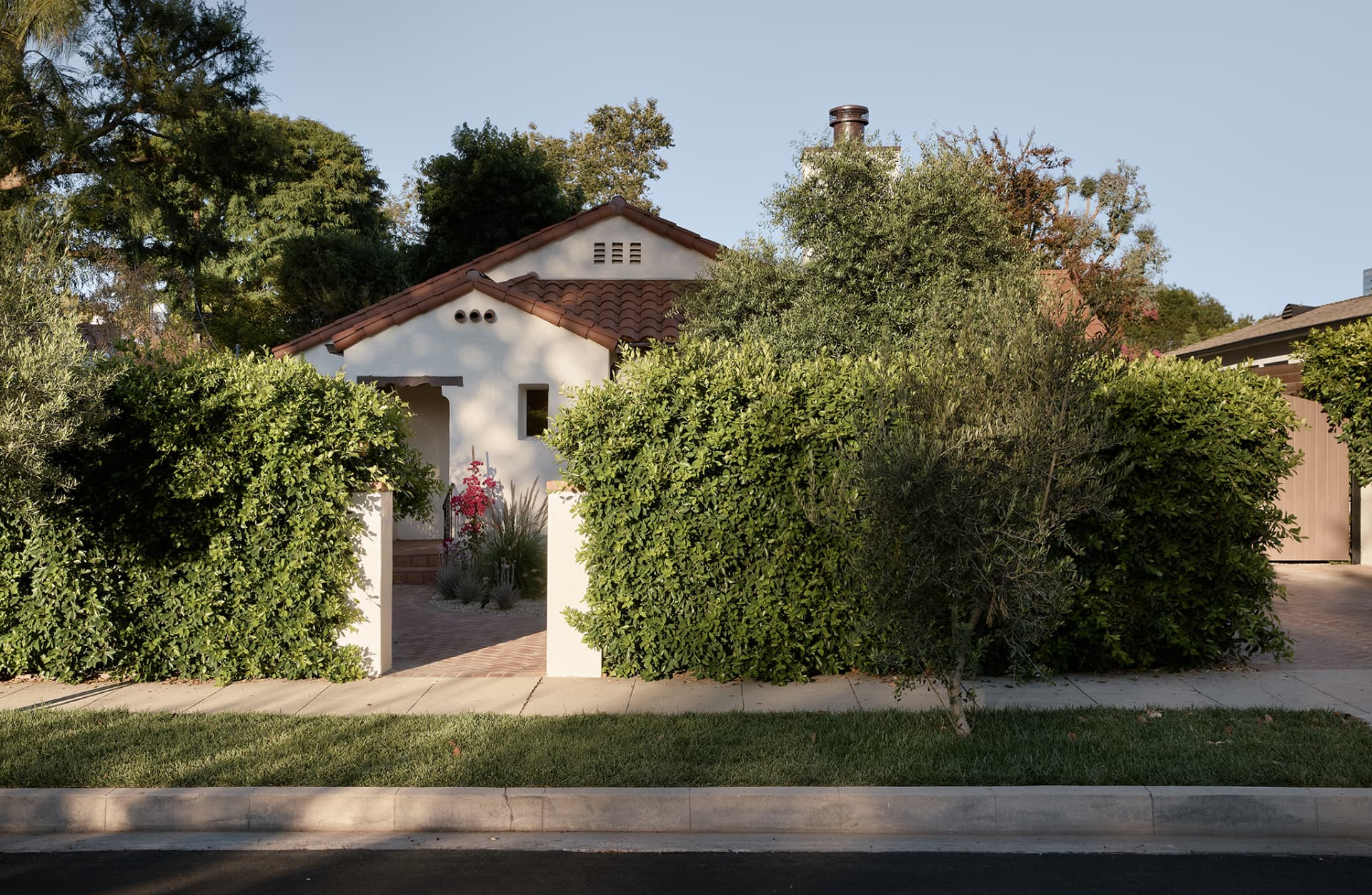 Street elevation of the restored Spanish residence behind clipped hedges and an olive tree