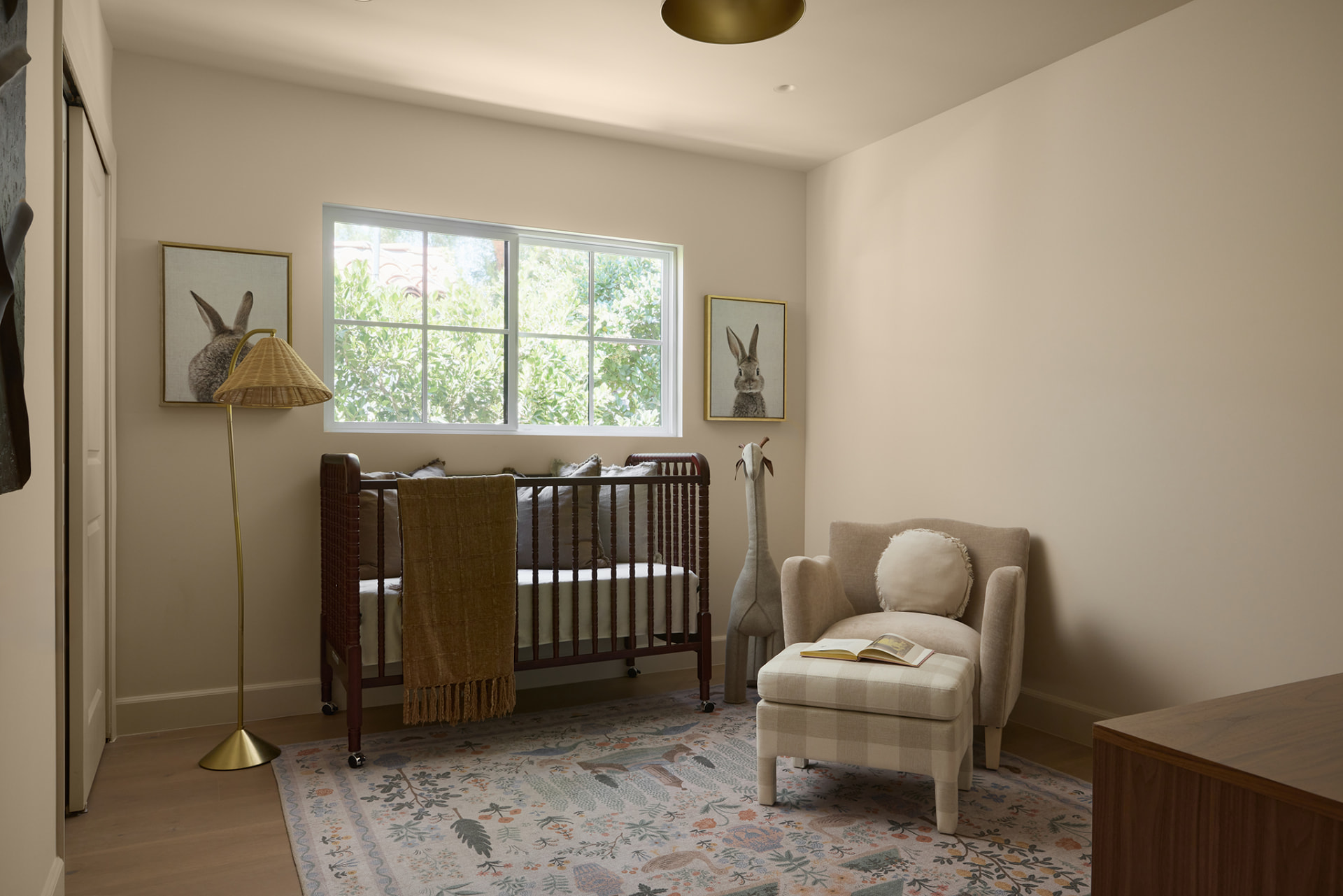 Nursery with a spindle crib, brass floor lamp, checkered ottoman and garden window