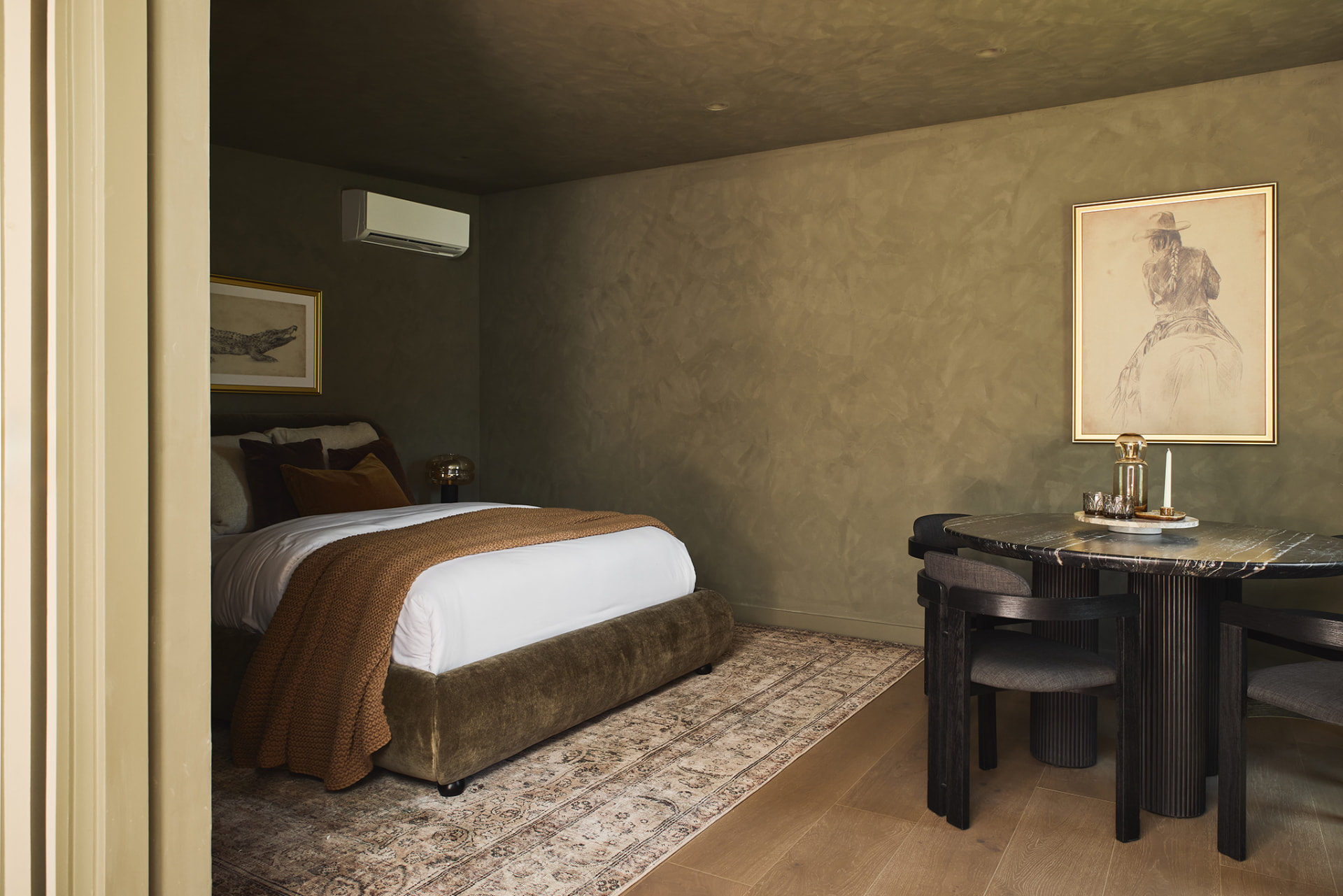 ADU bedroom and dining nook in olive limewash with a velvet bed, ochre throw and black marble table