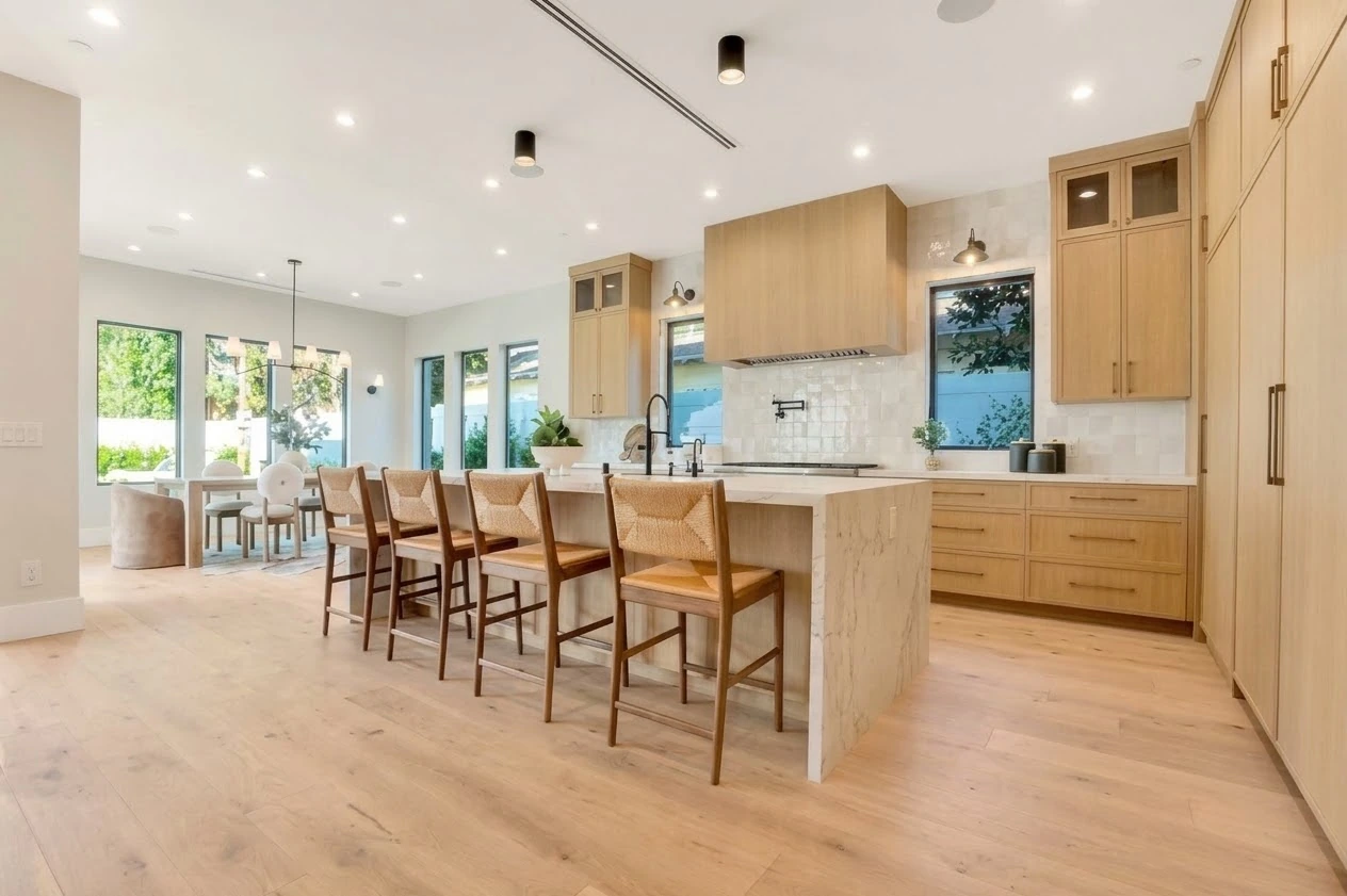Kitchen with oak cabinetry, a stone waterfall island, woven bar stools and garden-facing windows