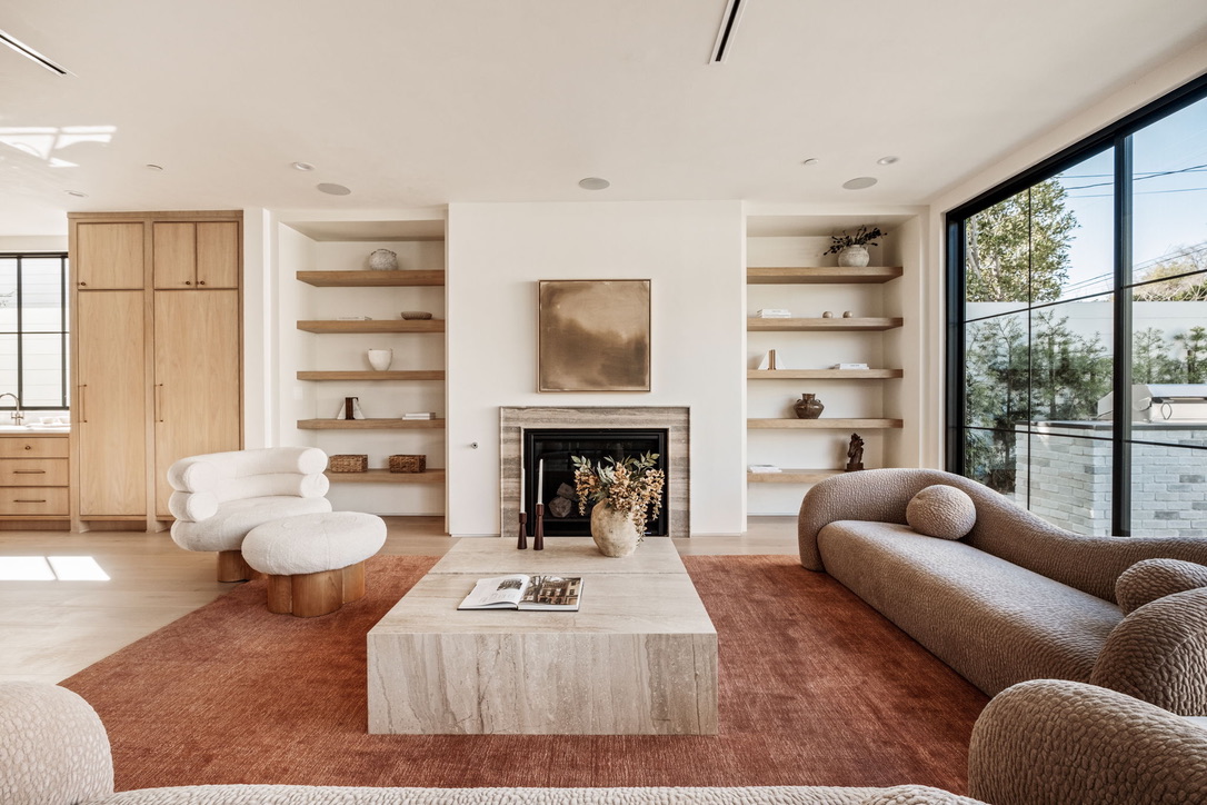 Living room with a stone fireplace, floating white oak shelving, bouclé seating and a deep terracotta rug