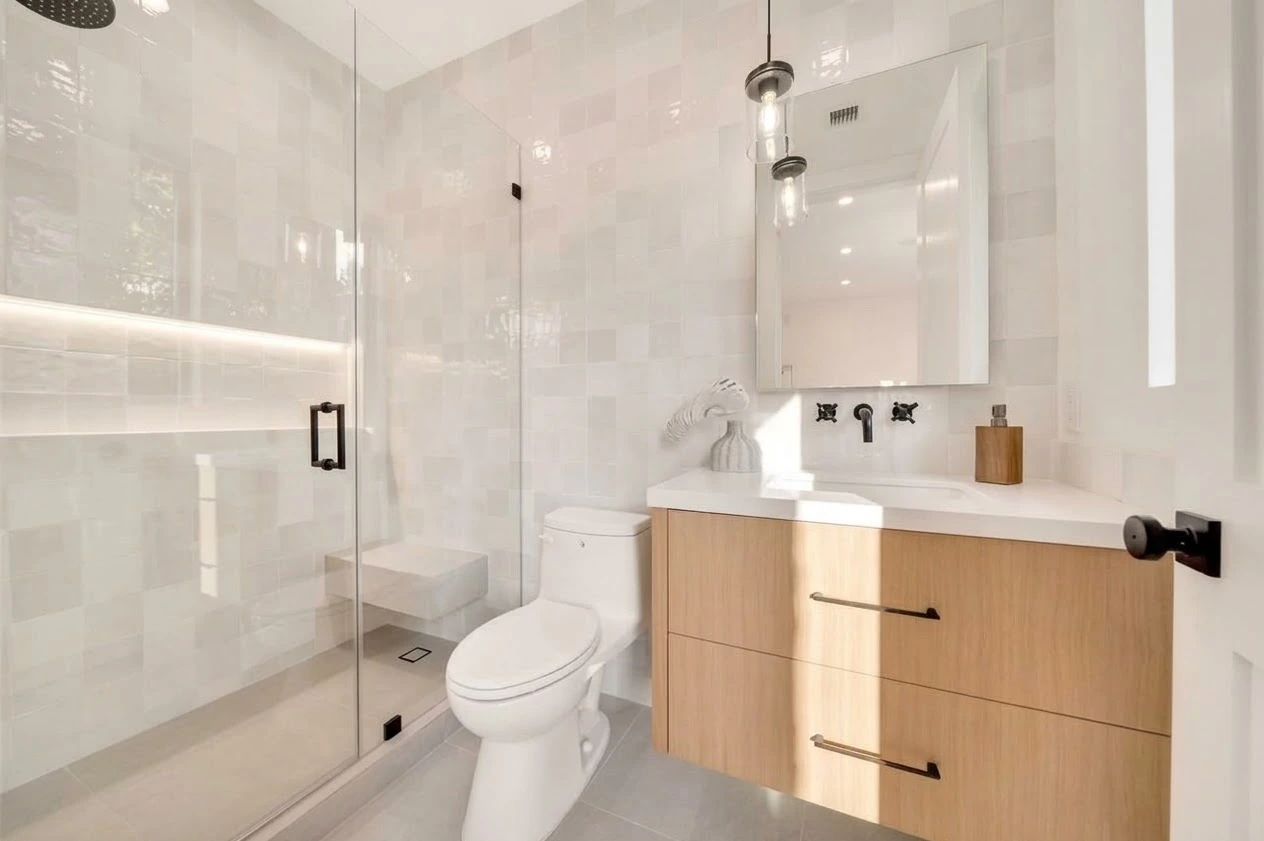 Bathroom with white tile walls, a floating oak vanity and a glass-enclosed shower with black fixtures