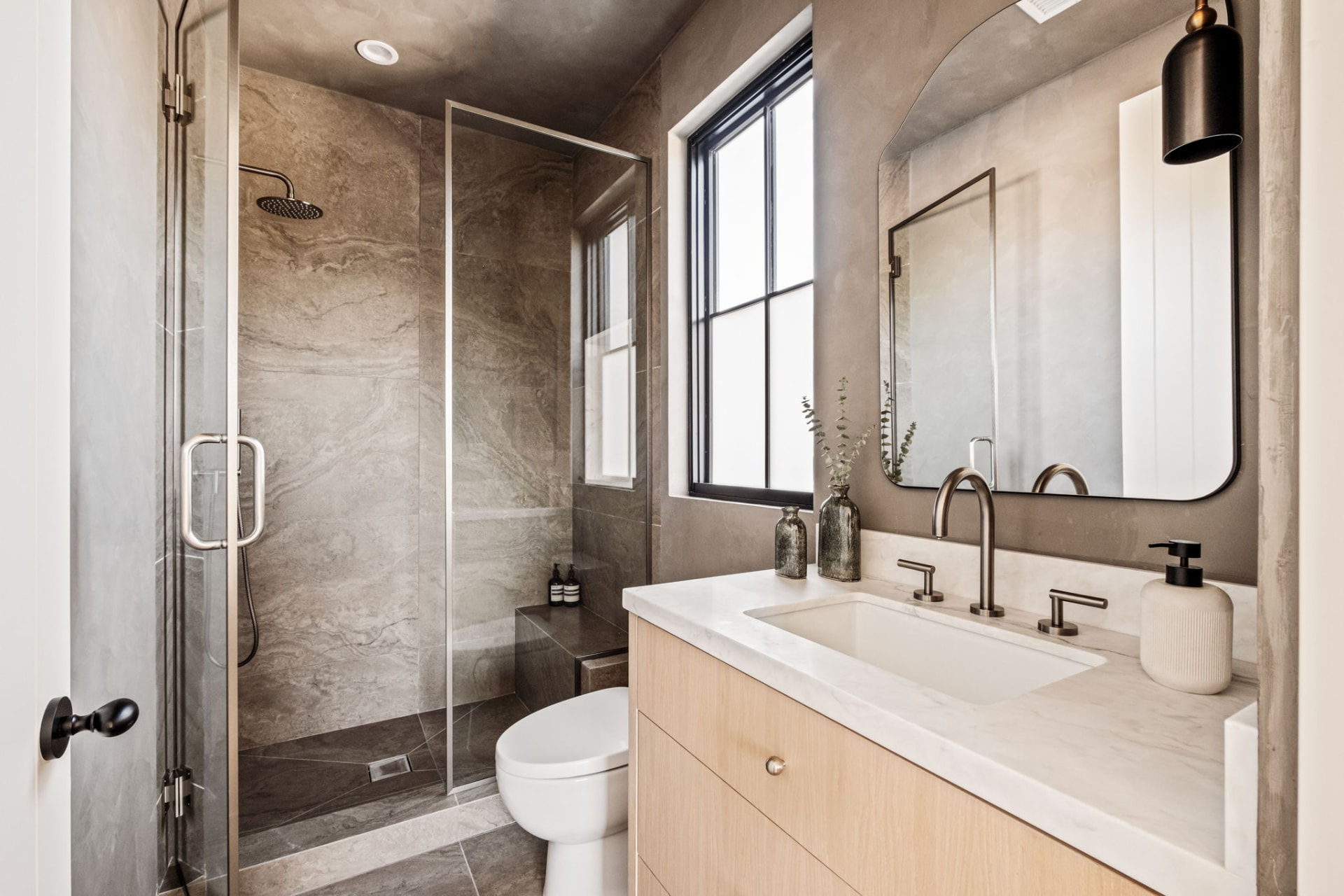 Bathroom in warm plaster with a large-format stone shower, oak vanity and bronze sconce