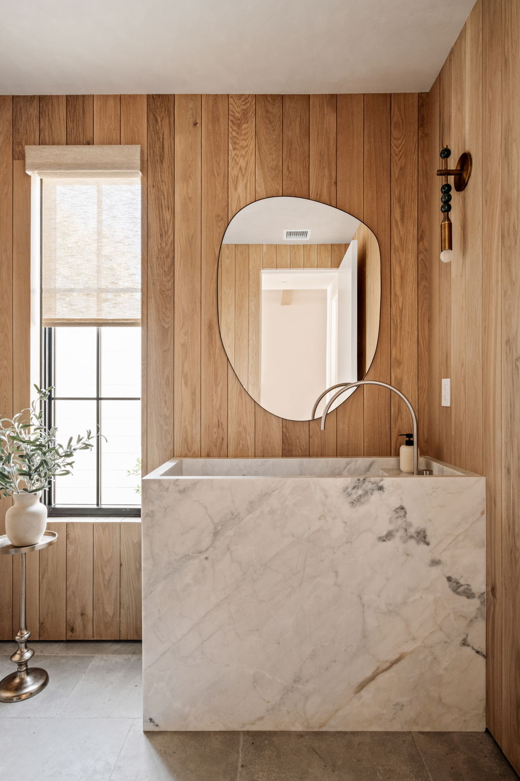 Powder room with white oak paneling, a solid marble sink block and an organic-shaped mirror