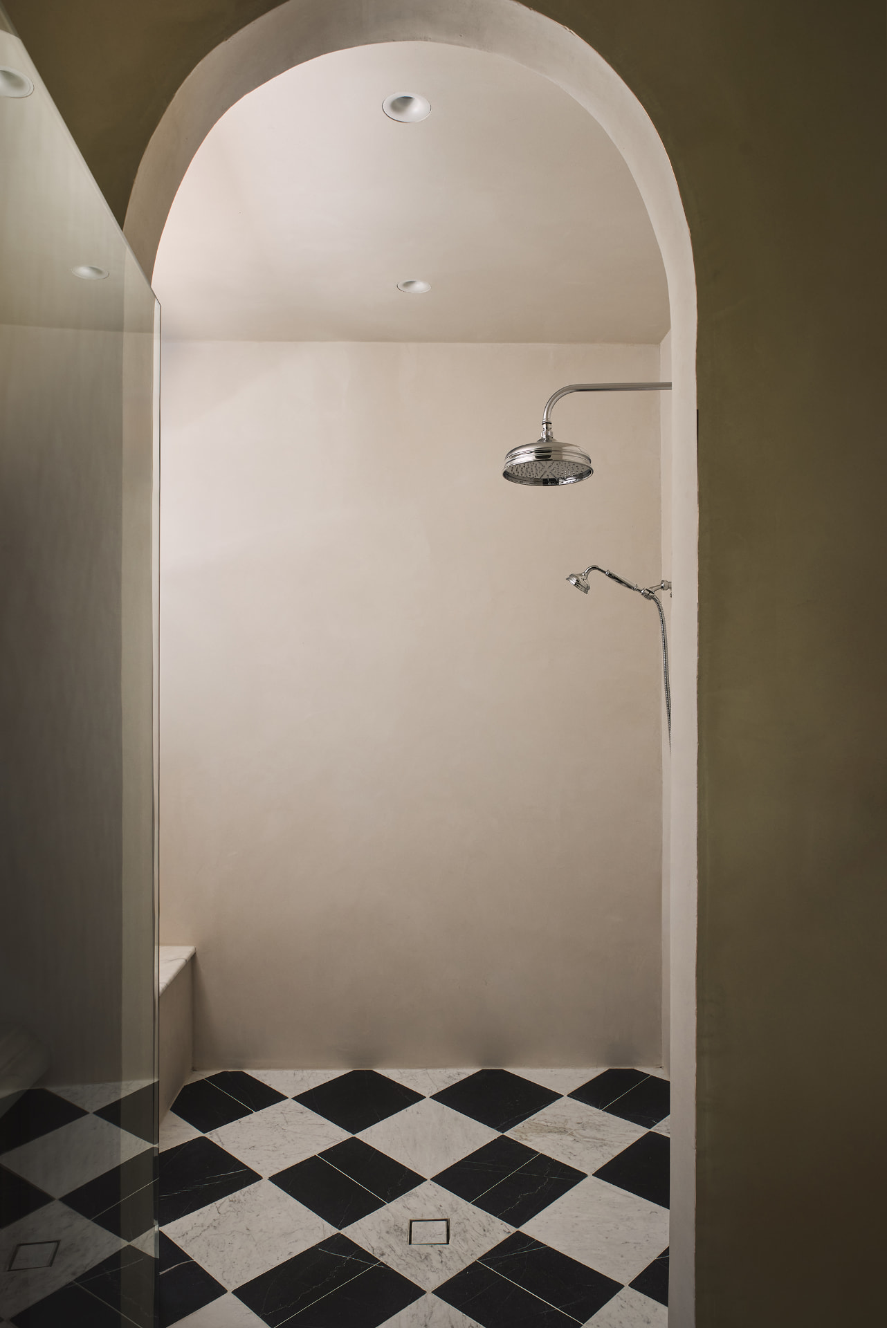 Arched limewash shower with a polished nickel rain head and checkered marble floor