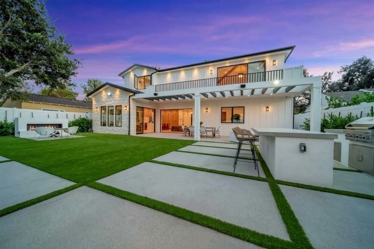 Rear elevation at dusk with a covered terrace, balcony, lawn, outdoor kitchen and fire pit