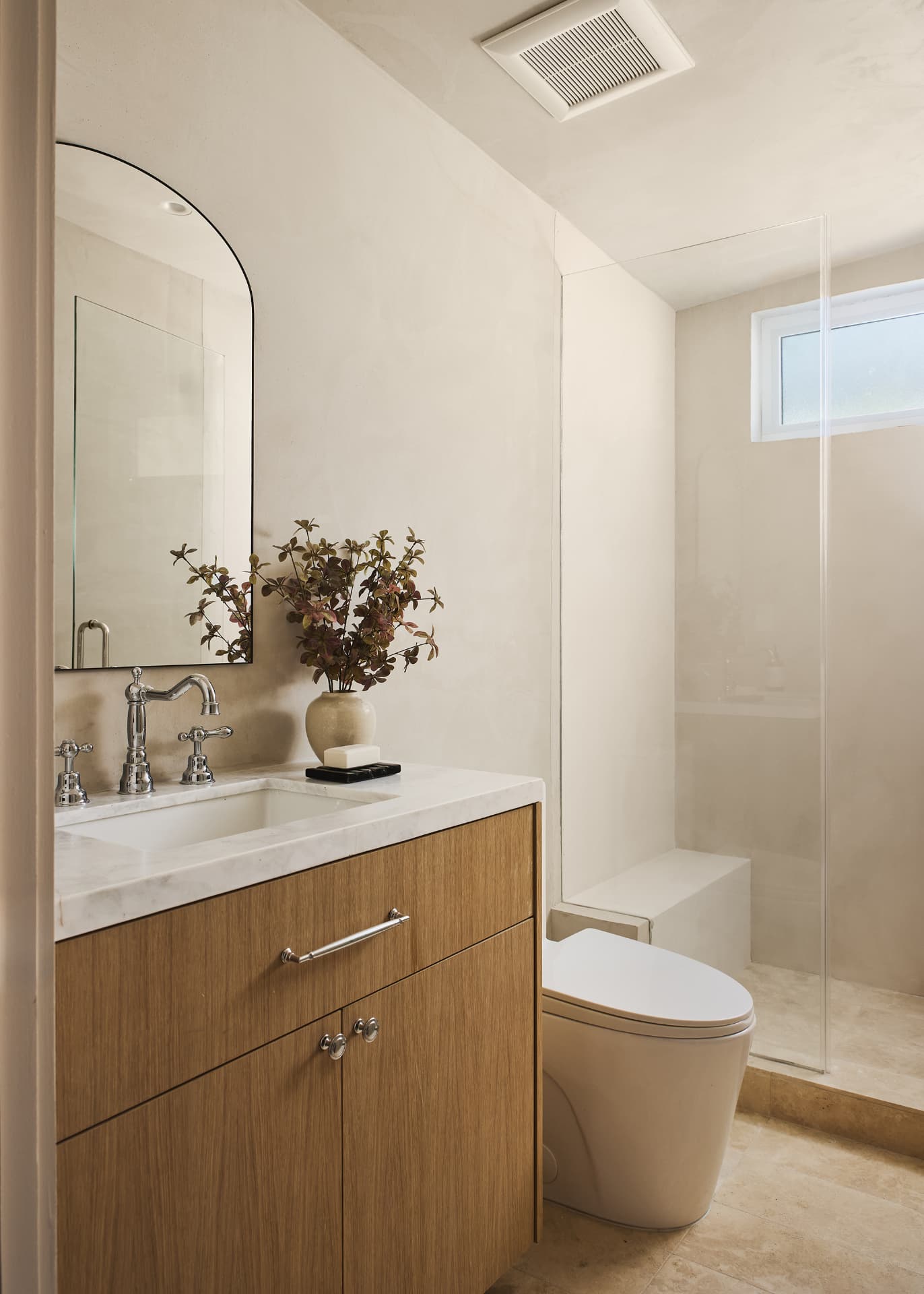 ADU bathroom in warm plaster with an arched mirror, oak vanity, marble counter and glass shower