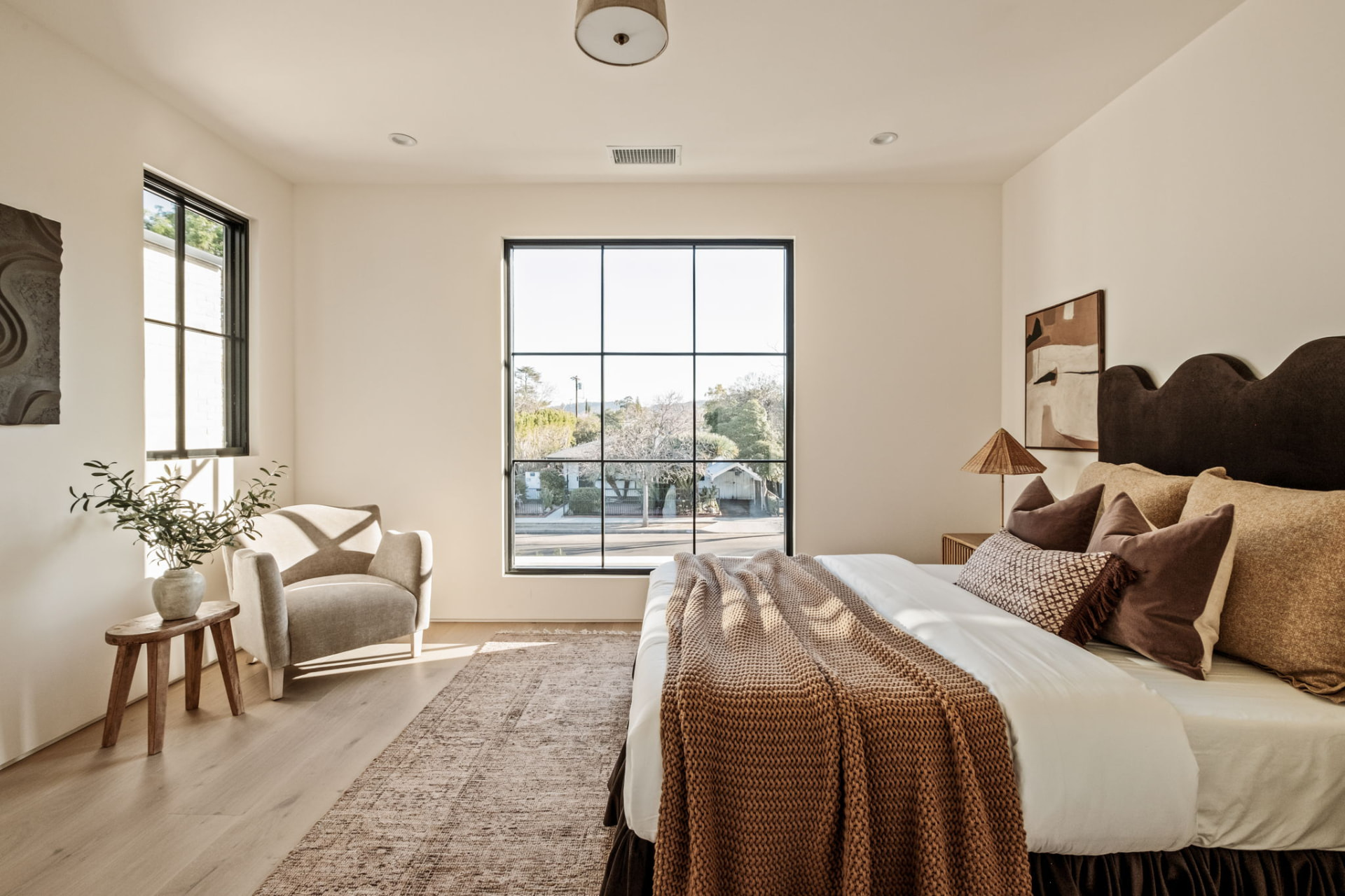 Primary suite with a scalloped brown velvet headboard, steel picture window and layered wool textiles