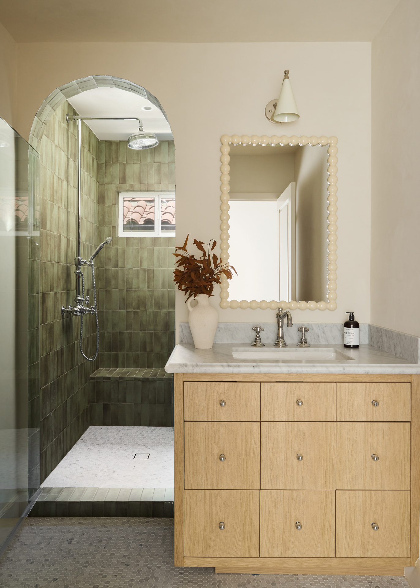 Bathroom with an arched green zellige shower, oak vanity and scalloped mirror