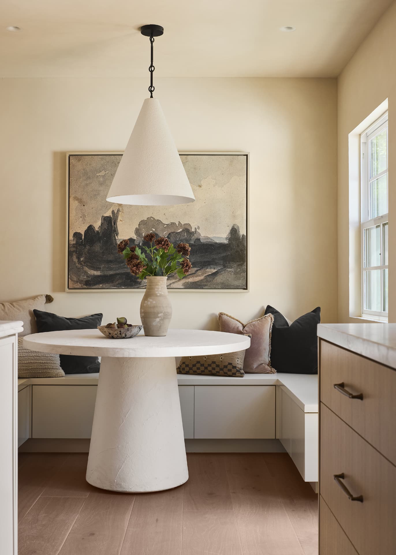 Breakfast banquette with a plaster pedestal table, cone pendant and vintage landscape painting