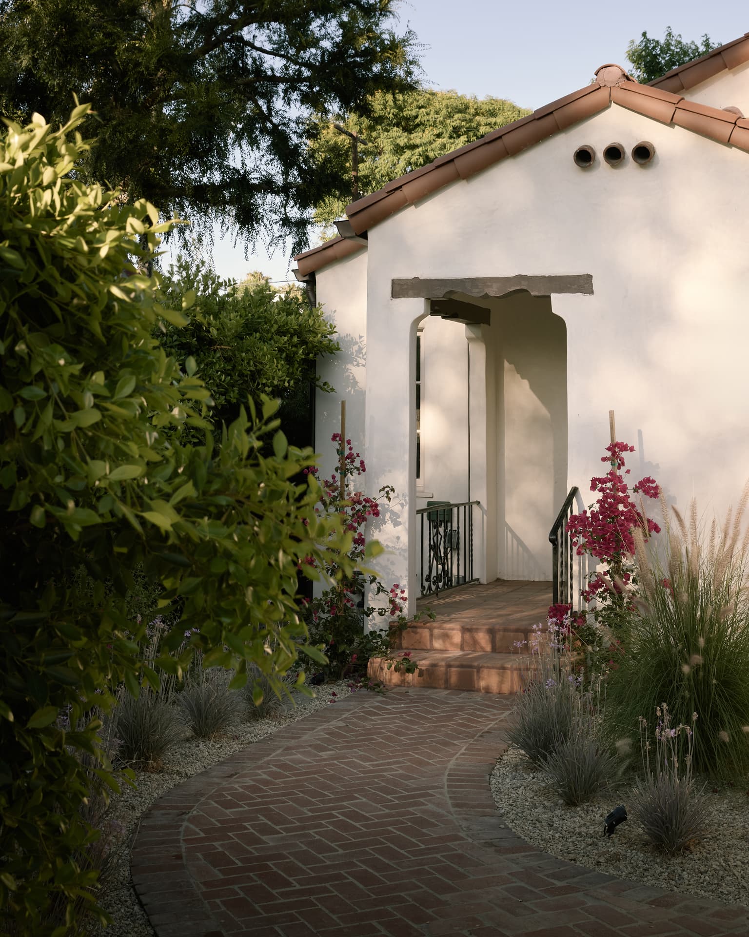 Front entry of the 1926 Spanish home with tile roof, arched porch, bougainvillea and a brick path