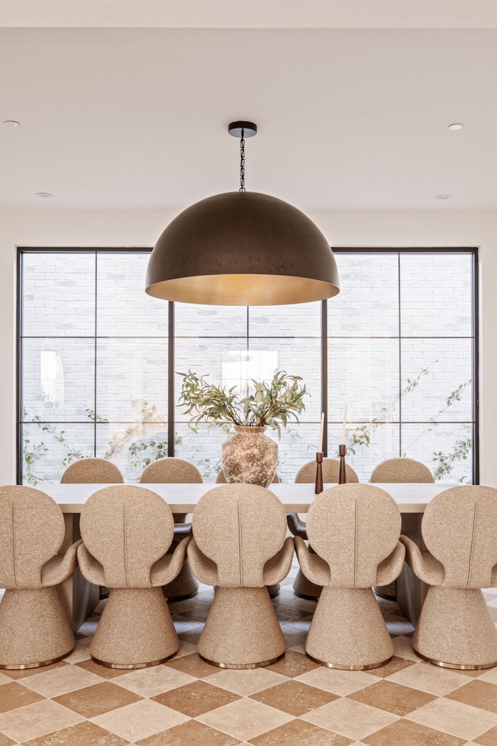 Dining table centred on a full-height steel window with climbing greenery against white brick beyond