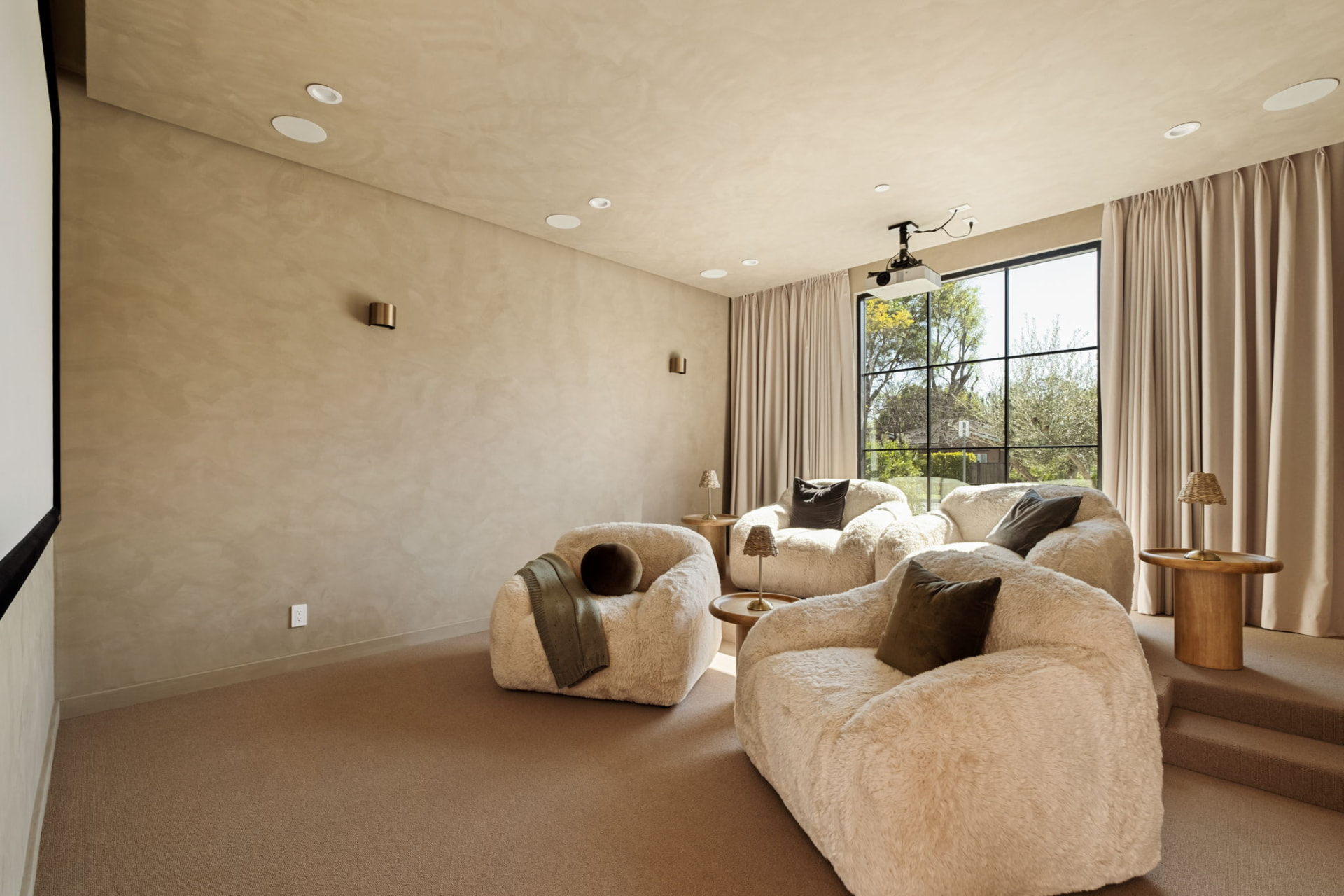 Media room with limewash plaster walls, oversized shearling lounge chairs and a projection screen
