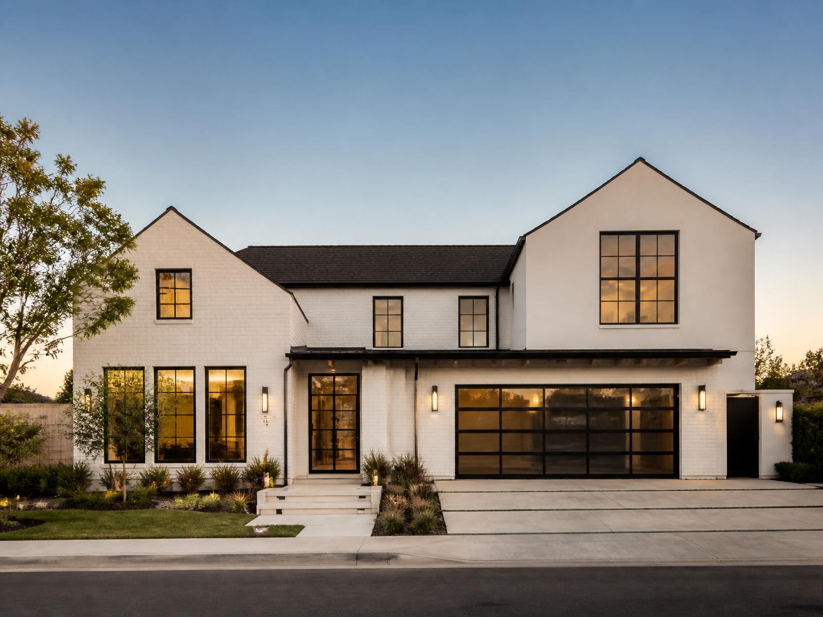 Newly built two-storey home at dusk with white brick, stucco gables and black steel windows